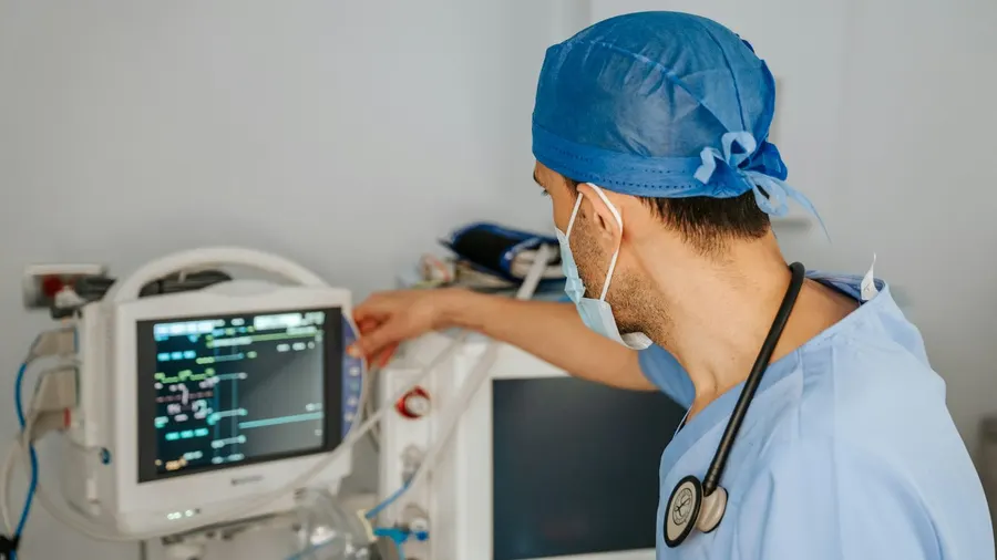 Médecin anesthésiste en tenue de bloc réglant un moniteur de surveillance